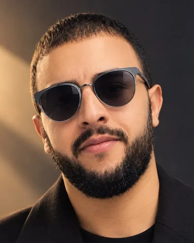 Abdeslam Hadiatallah, in warm gold light, wearing sunglasses and a dark coat.